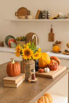 Bouquet of autumn flowers, books and pumpkins on table in light kitchen