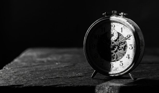 Vintage alarm clock in black and white on wooden surface showing time with visible gears and mechanism