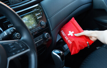 Close up of a hand holding a red first aid kit inside a modern car. Great for emergency preparedness, road safety, travel, vehicle equipment, insurance, and medical assistance concepts.