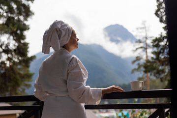 Fototapeta premium woman in a white robe and a towel on her head, with mountains in the background, in a hotel
