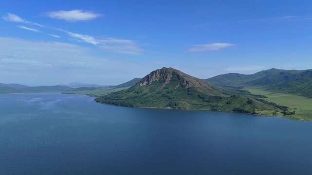 Majestic drone view of the deep blue Bukhtarma Reservoir and the opposite shore featuring a high mountain covered in dense evergreen forest. A clear summer day in East Kazakhstan highlights