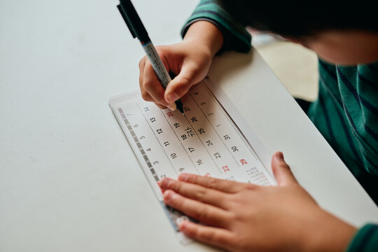 Asian elementary school student marking test date on calendar at home