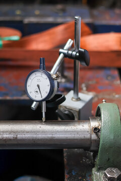 Mechanical engineer using dial indicator gauge to measure shaft runout and alignment on industrial machine in workshop