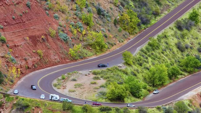 Aerial view of the famous switchbacks on the Zion-Mount Carmel Highway (State Route 9) in Zion National Park, Utah. The image captures vehicles, including cars and an RV, as they drive the dramatic, c