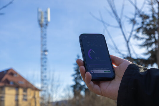 Szklarska Poreba, Poland - December 16, 2025: Hand holding smartphone displaying fast 5G mobile internet speed test results near a telecommunication tower