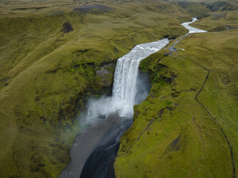 Aerial view of Skogafoss waterfall cascading dramatically through verdant hills, a powerful display of nature's artistry, Skogafoss, Rangarthing eystra, Iceland.