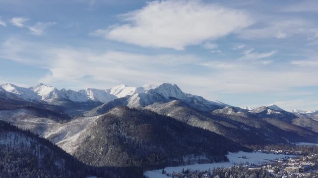 A breathtaking aerial drone shot of the Tatra mountain range above Zakopane, Poland, captured on a clear, sunny day. The footage focuses on the expansive mountain landscape, with rugged peaks, rolling