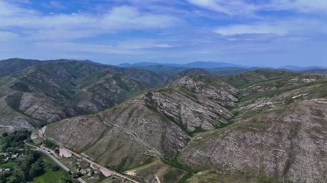 Cinematic drone footage featuring a sequence of low mountains partially covered with vegetation, stretching into the distance along the Bukhtarma Reservoir shore. The shot captures the unique terrain 