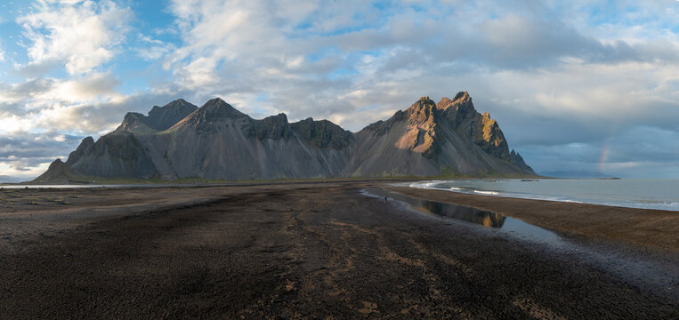 Aerial view of Vestrahorn mountain's jagged peaks meet the dark volcanic beach, reflecting the sky's soft hues, Hofn, Iceland.