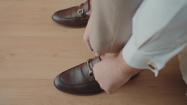 Person wearing brown leather horsebit loafers walking on light wood flooring