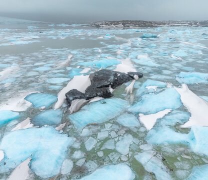 Aerial view of icebergs scattered across glacial lagoon waters, reflecting the sky's muted hues, creating a serene yet stark landscape, Oraefi, Sveitarfelagid Hornafjordur, Iceland.