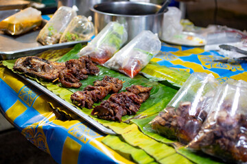 Obraz premium Street food skewers served on banana leaves with plastic takeaway bags and sauces. Authentic local market scene with grilled meat and traditional presentation.