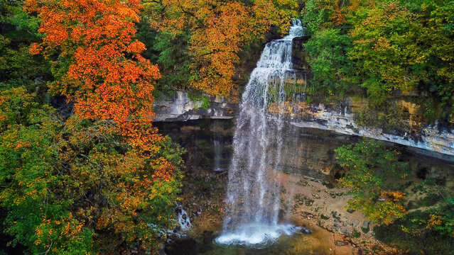 Aerial view of Herisson Waterfalls cascading down rugged cliffs surrounded by autumn foliage, a symphony of orange and green, Le Frasnois, Bourgogne-Franche-Comte, France.