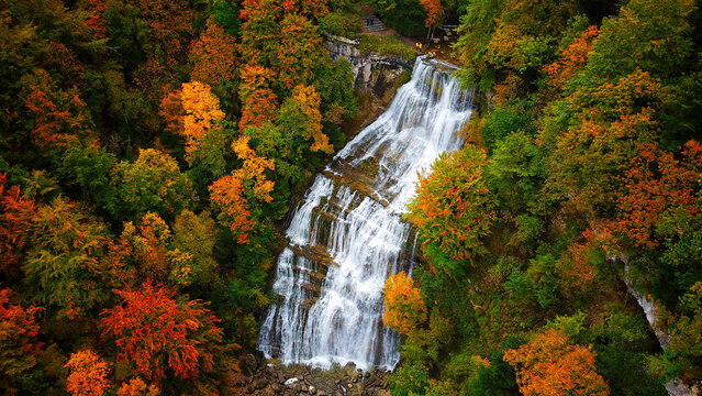 Aerial view of cascading waterfalls amidst a vibrant tapestry of autumn foliage, where oranges and greens blend in nature's artistry, Le Frasnois, Bourgogne-Franche-Comte, France.
