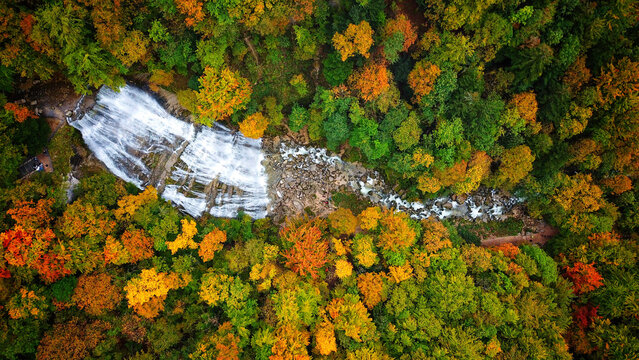 Aerial view of the cascading Herisson Waterfalls amidst the vibrant hues of autumn foliage, a tapestry of green, gold, and russet, Le Frasnois, Bourgogne-Franche-Comte, France.