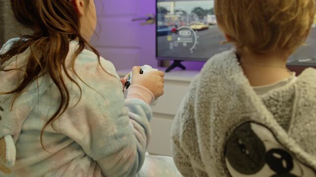 Close-up of delighted brother and sister playing video games together. They sit comfortably holding controllers, full of laughter and excitement during their gaming session at home 4K.