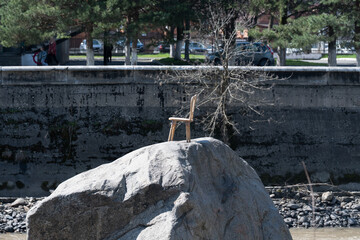 Surreal scene with a small wooden chair standing alone on top of a large boulder in a river. © alan