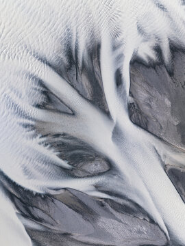 Aerial view of glacial rivers carving intricate patterns across the landscape, a dance of icy whites and stony greys, Lake Tekapo, New Zealand.