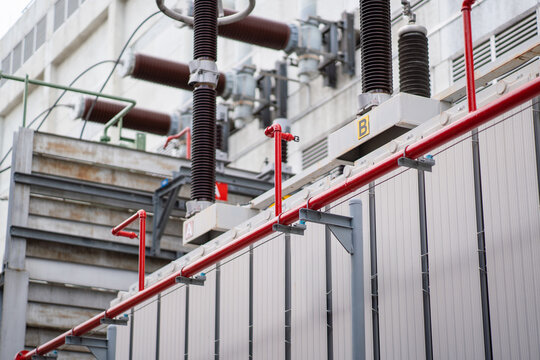 Close-up of transformer cooling fins with red fire protection piping and high voltage bushings, showing substation safety infrastructure and outdoor electrical equipment.