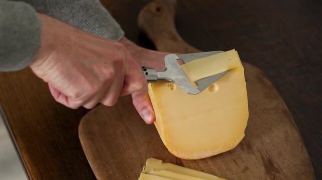 Cutting Dutch cheese with a traditional cheese slicer on wooden board