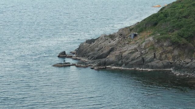 Lone man living off-grid in a makeshift coastal shelter on a rugged rocky shore