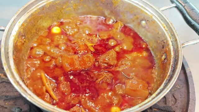 Close-up of boiling Thai Northern style pork curry (Gaeng Hung Ley) with ginger and spices in a stainless steel pot.