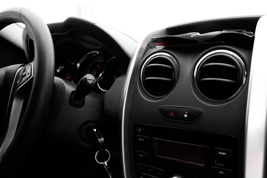 Interior of a modern car showing the dashboard with round air vents, steering wheel, and ignition key in black and white minimalist style, close up view for automotive, travel, and transport concept