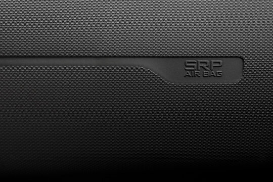 Macro shot of an SRP Airbag sign embossed on a black textured car dashboard in minimalist black and white style for automotive safety, vehicle interior and transport technology concept