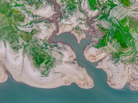 Aerial view of the interplay of turquoise waters and sun-baked earth, a tapestry woven with verdant fields, Chakswari, Azad Kashmir, Pakistan.
