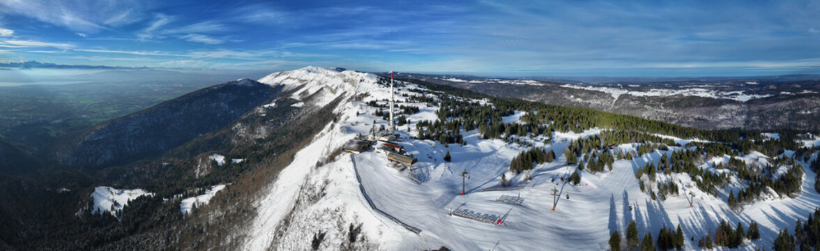 Aerial view of snow-covered slopes and dark green forests meet under a vast blue sky at the ski resort, Gex, Auvergne-Rhone-Alpes, France.