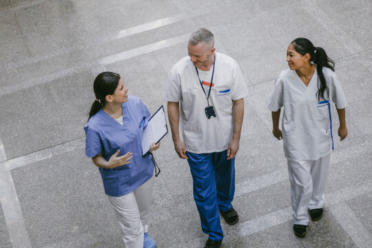 High angle view of smiling female nurse discussing with doctors while walking in hospital lobby
