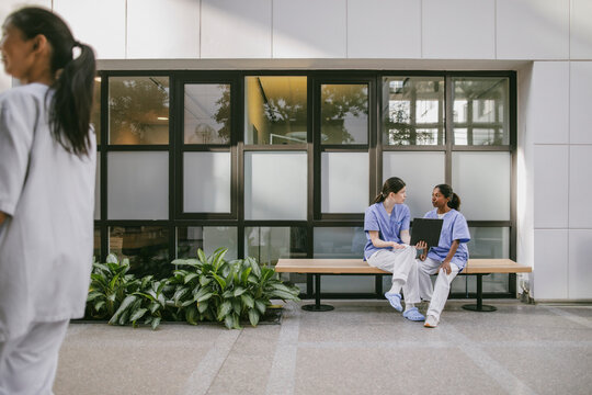 Female healthcare professionals discussing medical documents while sitting on bench in hospital