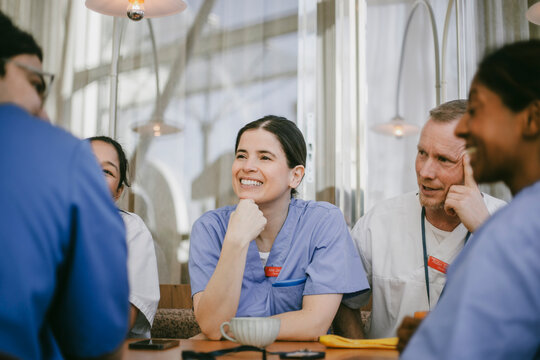 Smiling female doctor leaning on elbow spending leisure time with coworkers at coffee break in hospital cafeteria