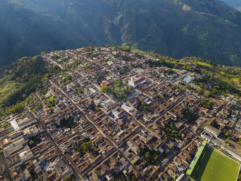 Aerial view of terracotta rooftops sprawling across the landscape, punctuated by a central church, nestled amidst verdant hills, Salamina, Caldas, Colombia.