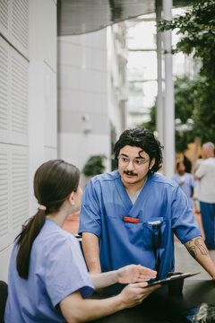 Young male physician talking with female nurse explaining medical documents in hospital