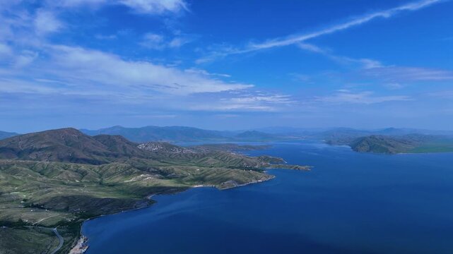 Grand aerial drone view of the vast blue Bukhtarma Reservoir, framed by picturesque hilly and mountainous shores. The footage captures the majesty of East Kazakhstan's nature on a bright summer day. 