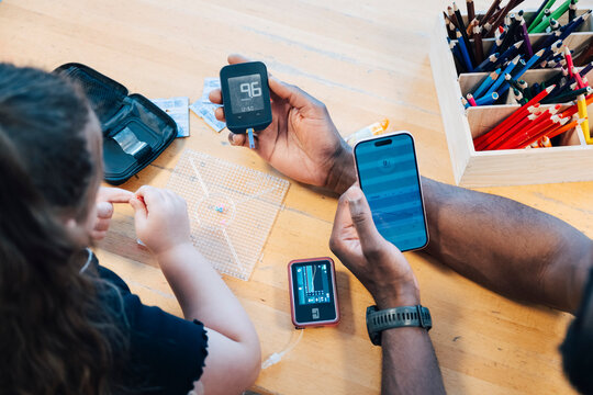 High angle view of teacher using smart phone to track health data for child with chronic condition
