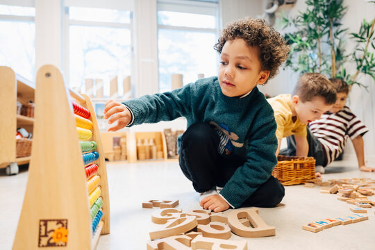 Boy playing with colorful wooden abacus while sitting on classroom floor at preschool