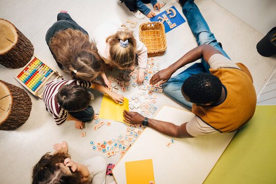 Directly above view of teacher assisting students playing with letter blocks while sitting on classroom floor