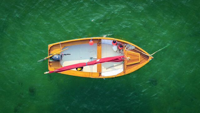 Aerial view of a wooden boat with a red sail contrasts against the emerald water, creating a vivid scene of maritime beauty, Carantec, Brittany, France.