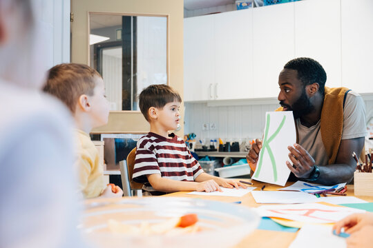 Mature male teacher playing creative alphabet learning game with kindergarten students