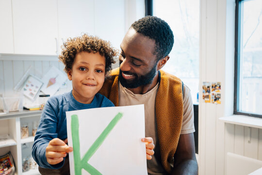 Portrait of boy holding letter K next to male teacher in kindergarten classroom