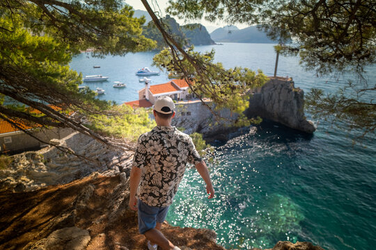 View of man in floral shirt standing on cliff with panoramic view of green hills and sparkling blue Adriatic Sea Petrovac Riviera