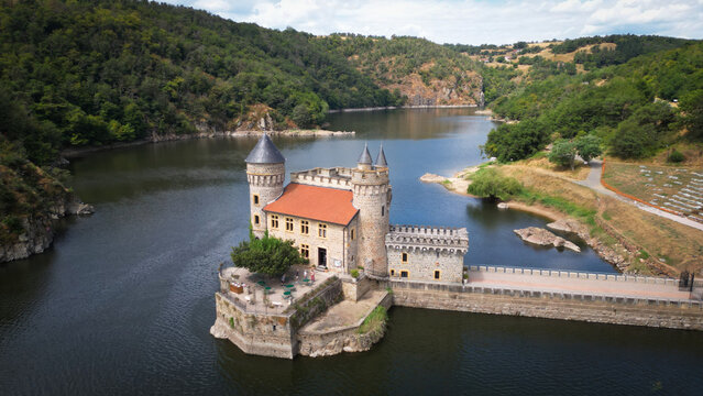 Aerial view of the Chateau de la Roche standing majestically in the glistening water, surrounded by lush green hills, Saint-Priest-la-Roche, Auvergne-Rhone-Alpes, France.