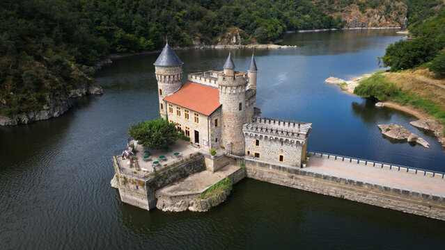 Aerial view of the Chateau de la Roche, a stone fortress with a red-tiled roof, rises majestically from the tranquil waters, Saint-Priest-la-Roche, Auvergne-Rhone-Alpes, France.
