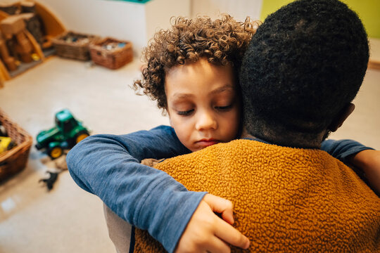 Sad boy with curly hair embracing male teacher in classroom