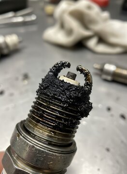 Old spark plug with heavy carbon buildup and burnt electrodes