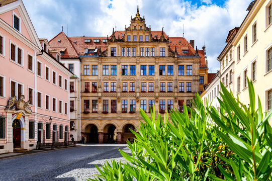 Historic town hall at the Untermarkt in G&ouml;rlitz with richly decorated renaissance facade, arcades, red roof tiles, cobblestone pavement and green plants in the foreground.