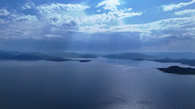 A mesmerizing drone view of the Bukhtarma Reservoir captured in backlight. Powerful sunbeams pierce through thick clouds, creating a dramatic lighting effect over the vast water surface. This summer 