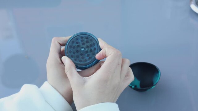 Hands holding and using a blue herb grinder to crush medical marijuana for recreational use
